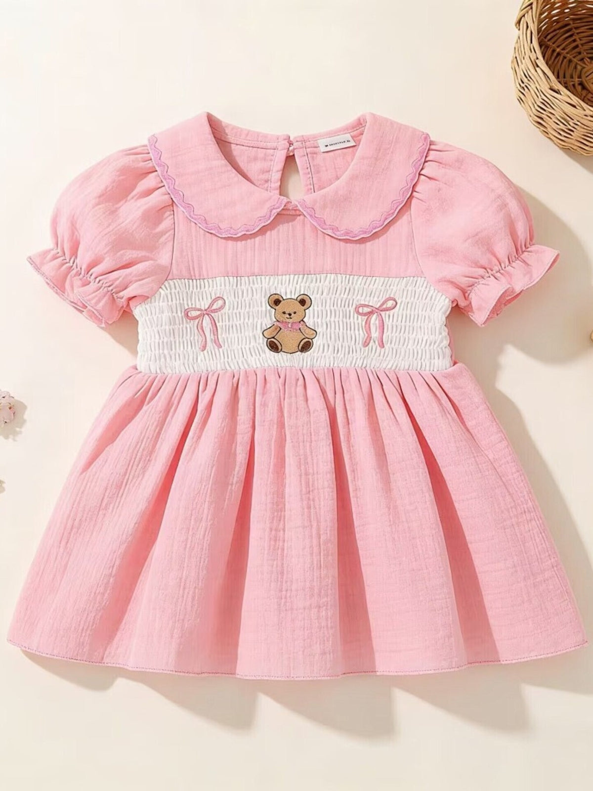 Pink baby dress with smocked bodice, teddy bear embroidery, Peter Pan collar, and puff sleeves.