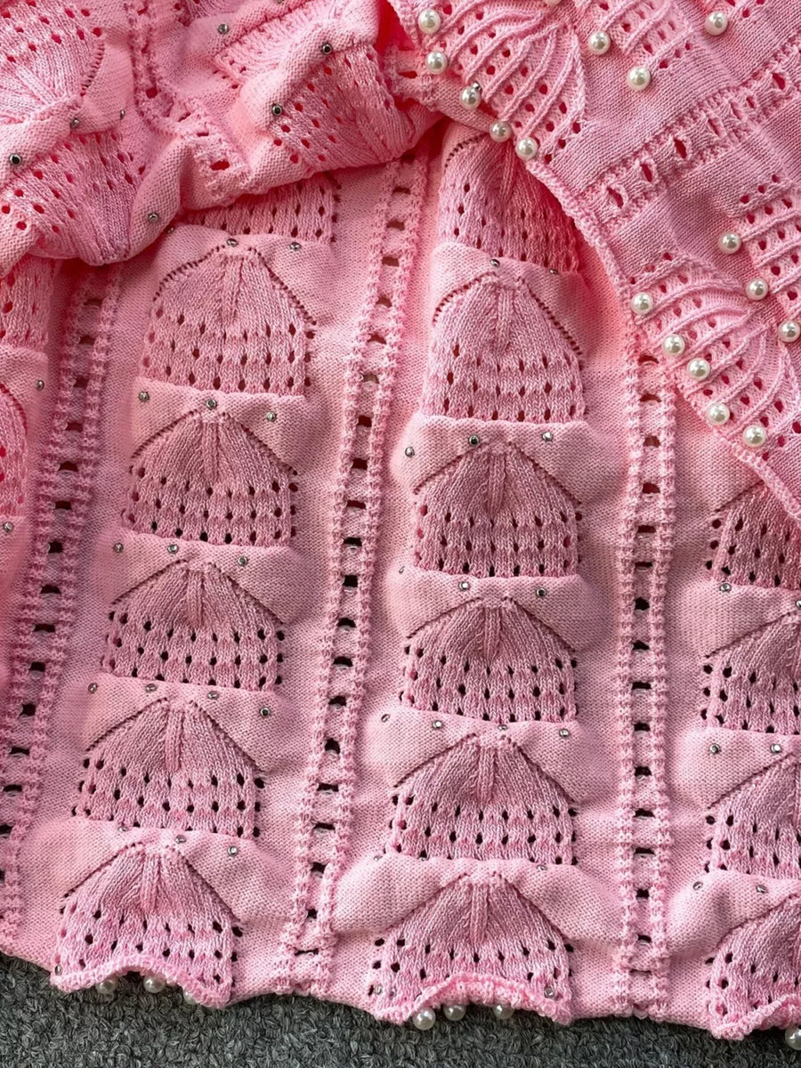 Pink knit midi dress with textured pattern, cutouts, and pearl embellishments.
