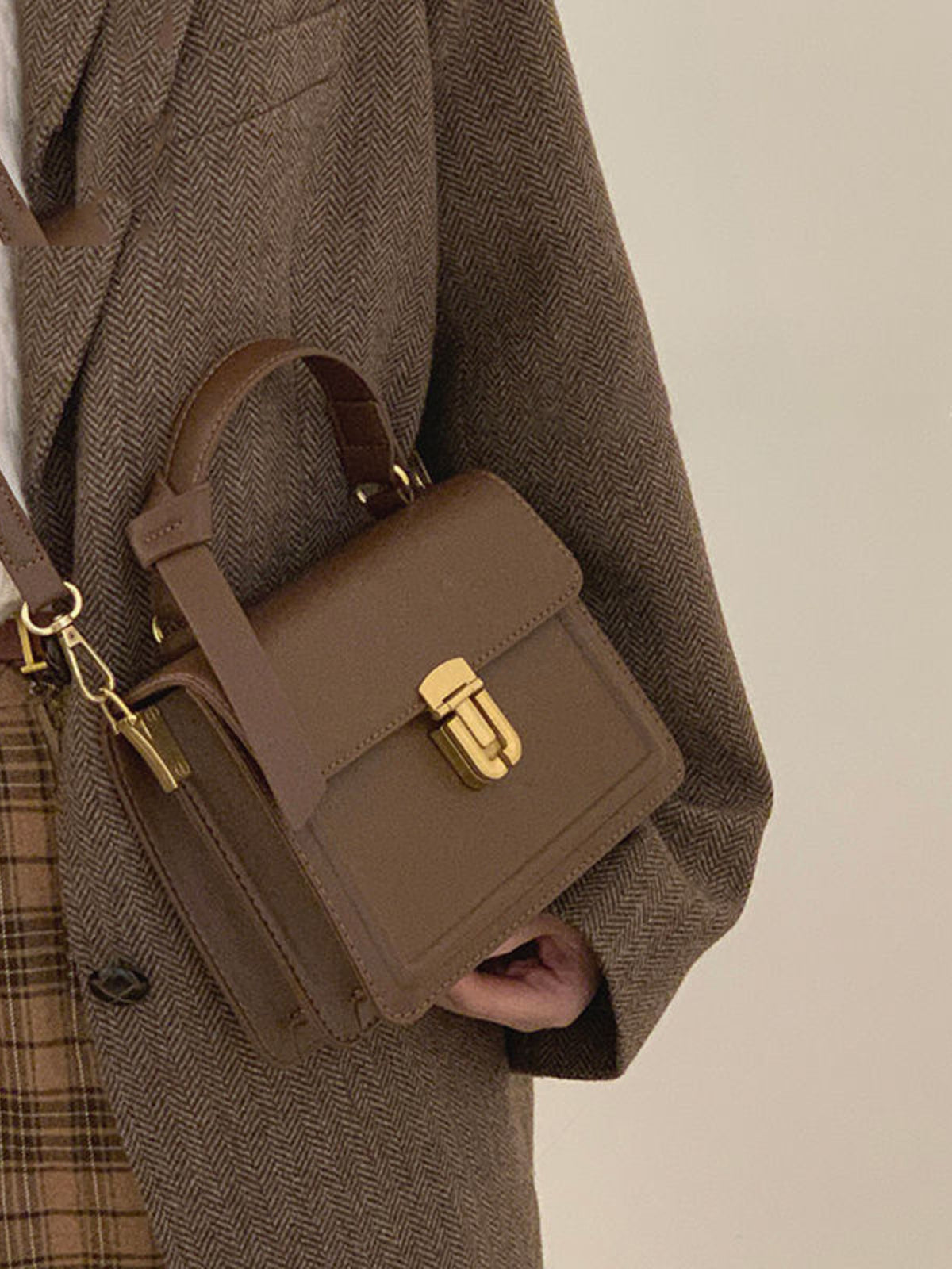 Small coffee pu leather crossbody bag with gold turn-lock closure and top handle.