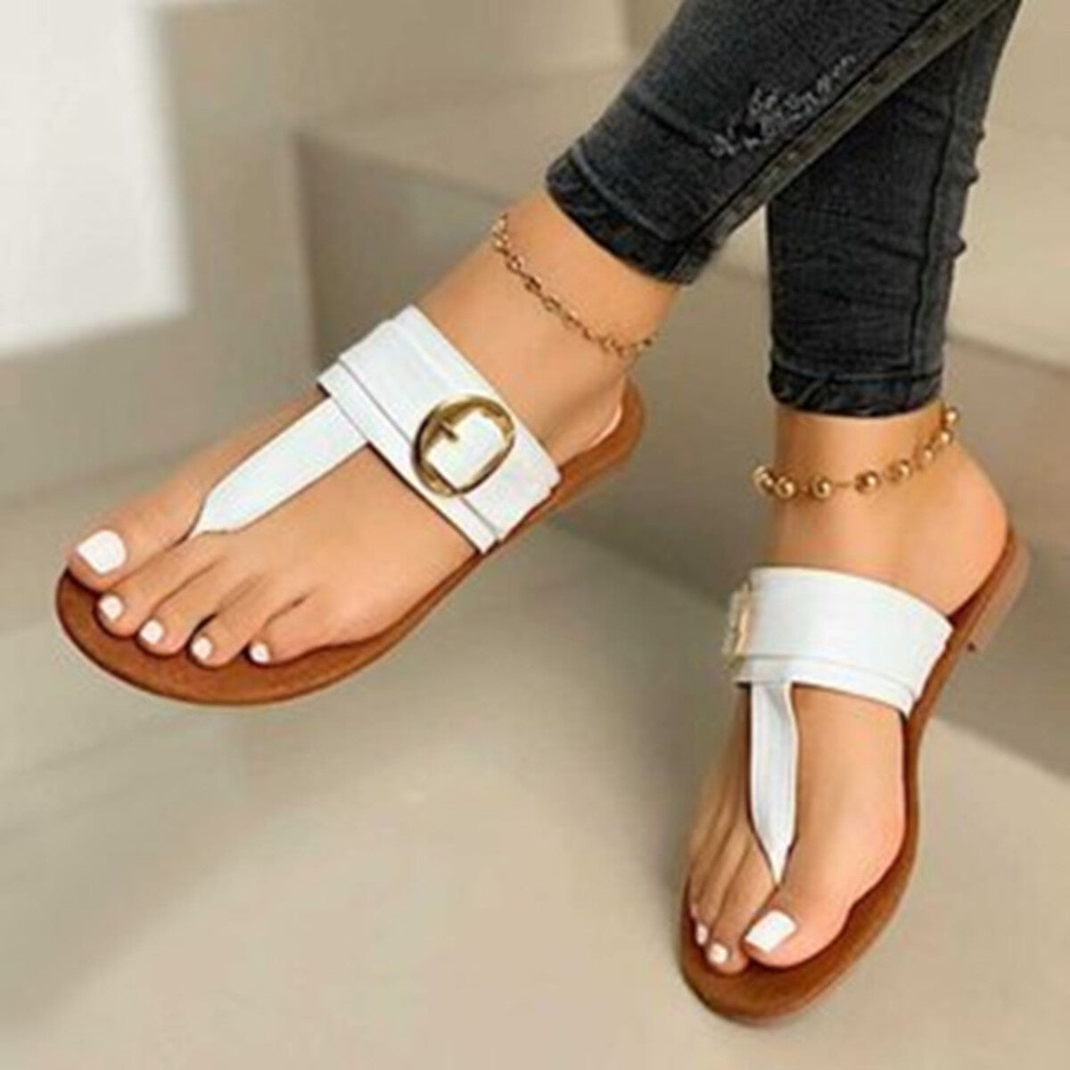 White toe-post sandals with gold buckle detail and flat sole.