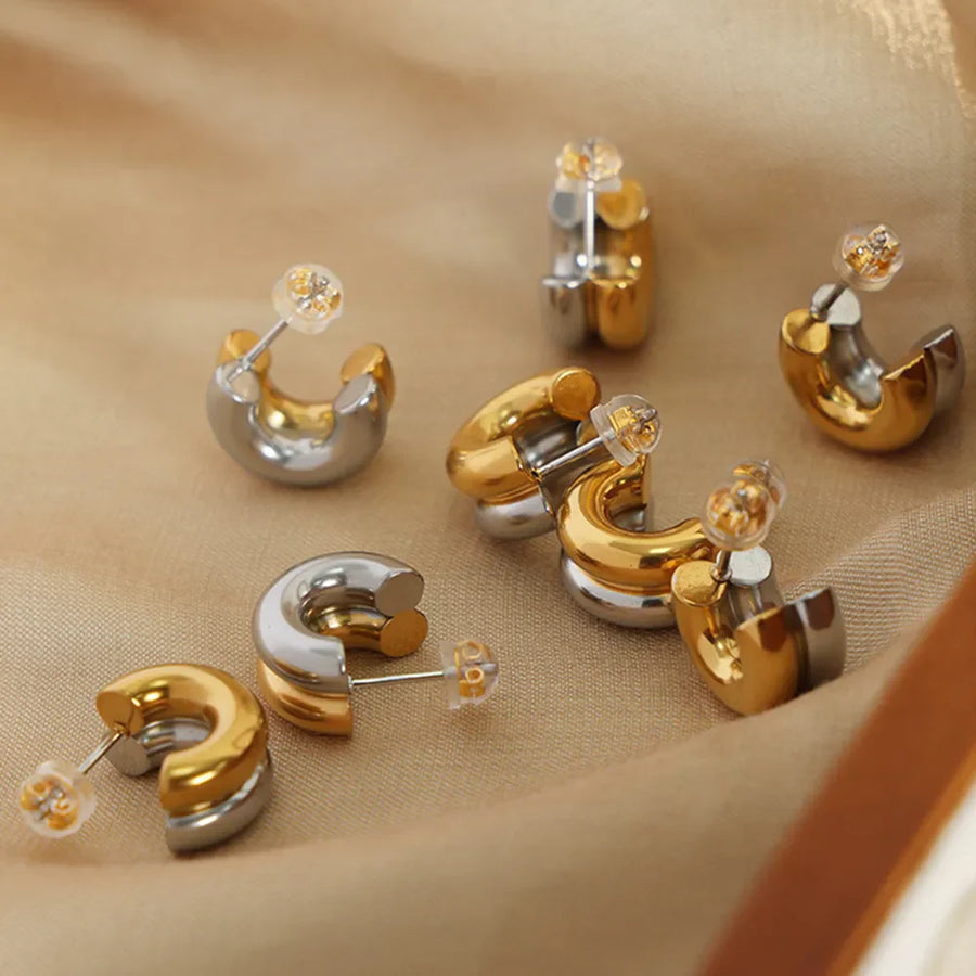 Dual-tone sculptural C-hoop earrings in gold and silver feature a modern, curved design.