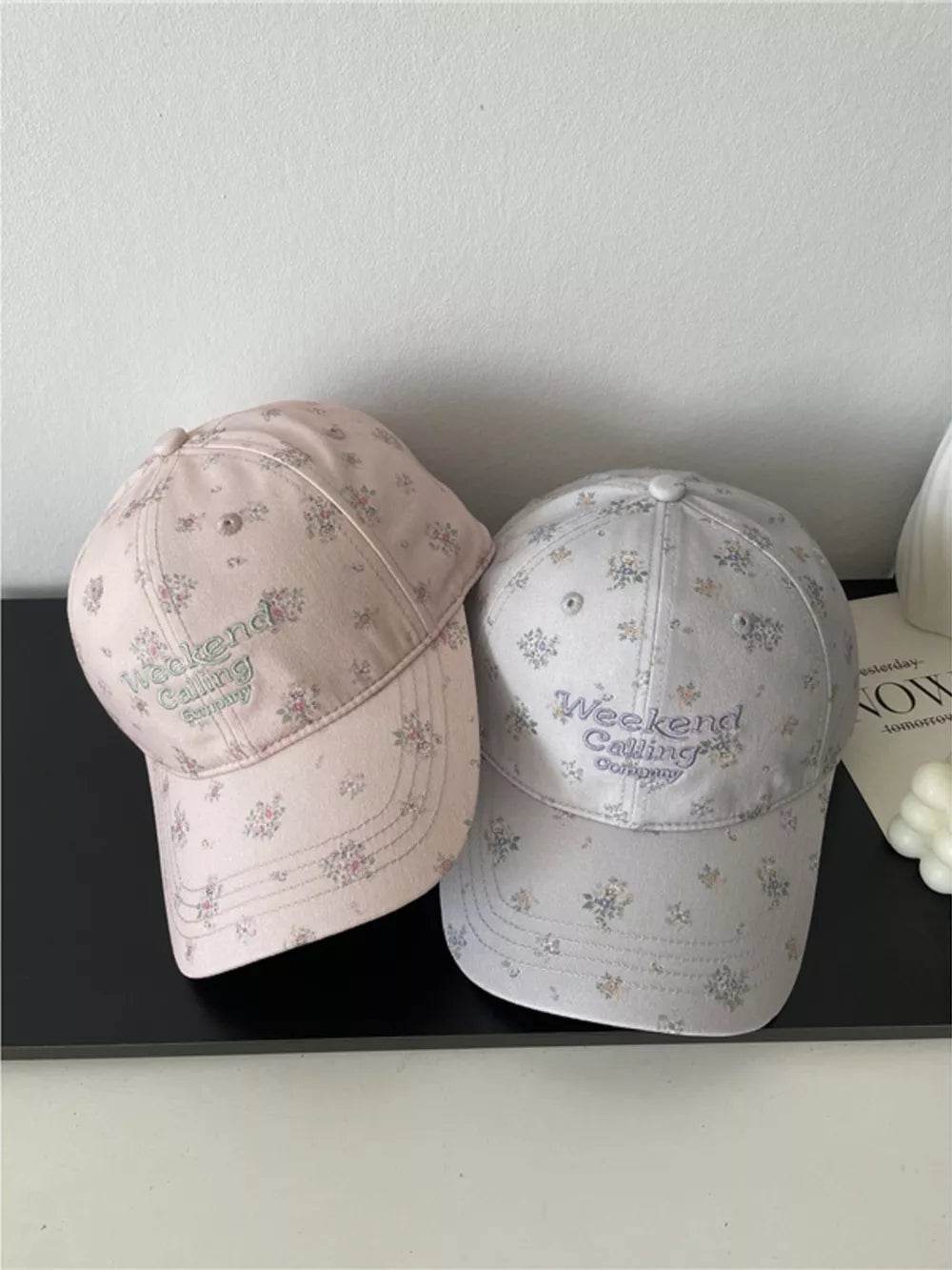 Embroidered floral baseball caps in pink and light gray with "Weekend Calling Company" text.