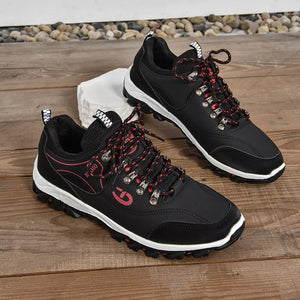 Black lace-up low-top sneakers with patterned red and black laces and pink accents.