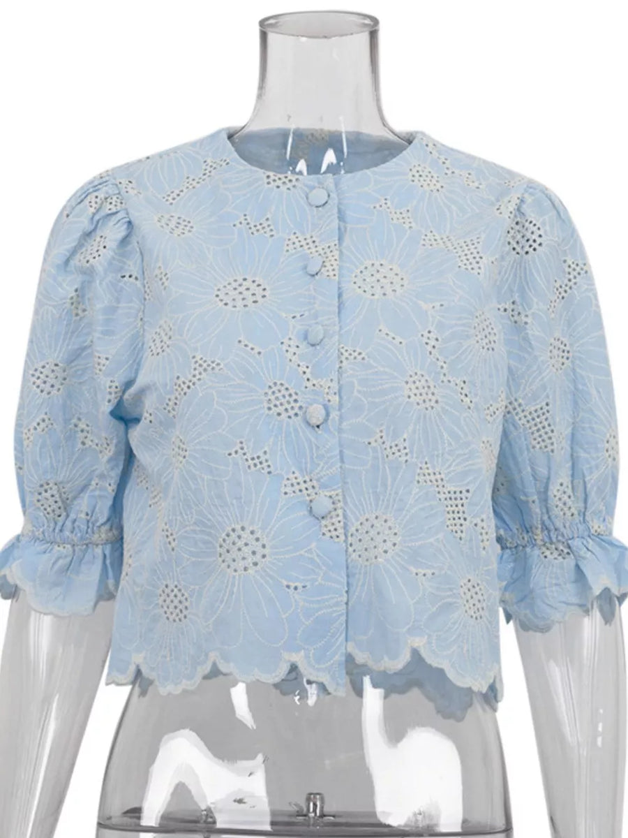 Blue eyelet blouse with floral embroidery, puff sleeves, and ruffled cuffs.