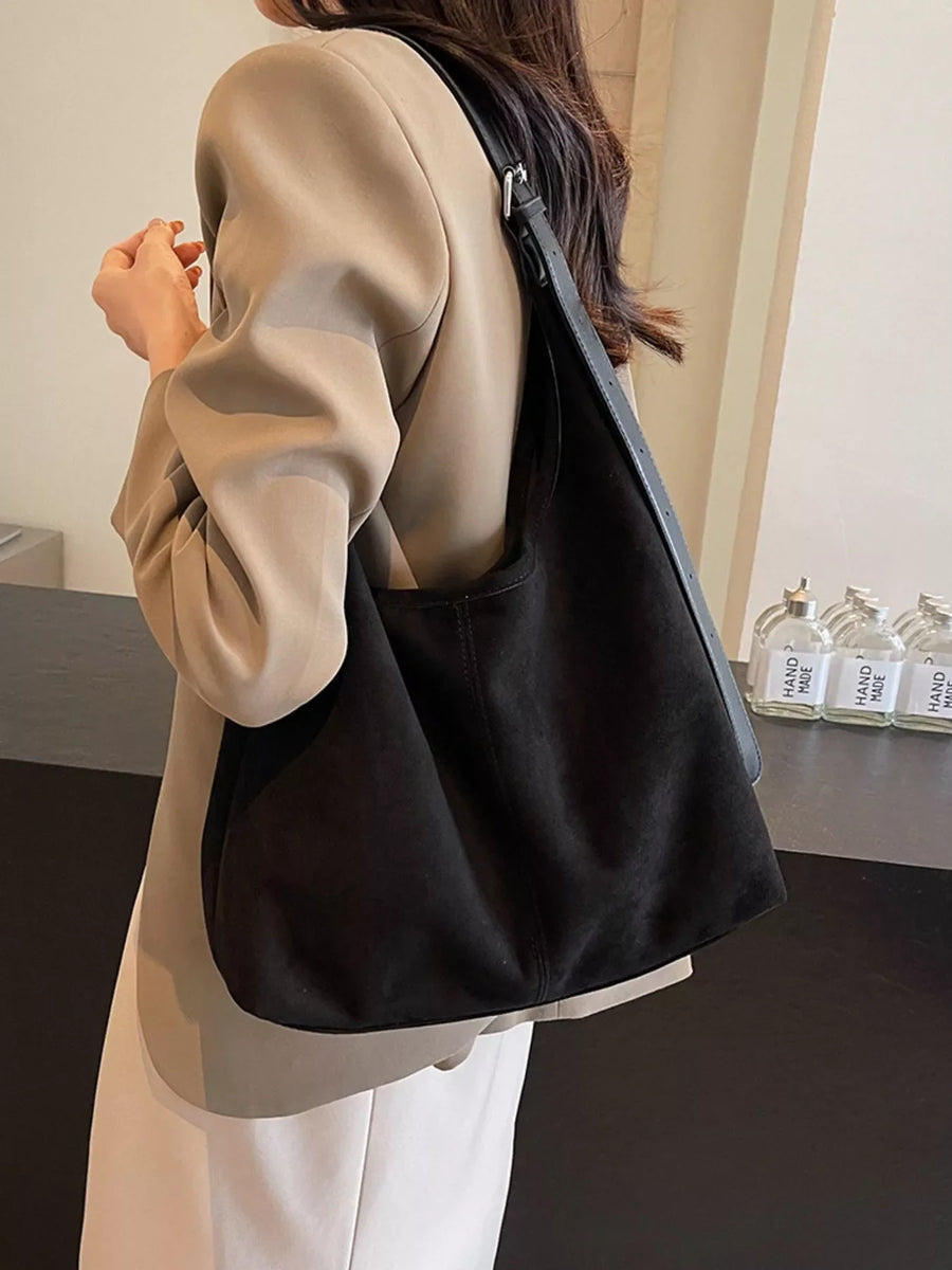 Black suede hobo bag with adjustable strap, worn casually.
