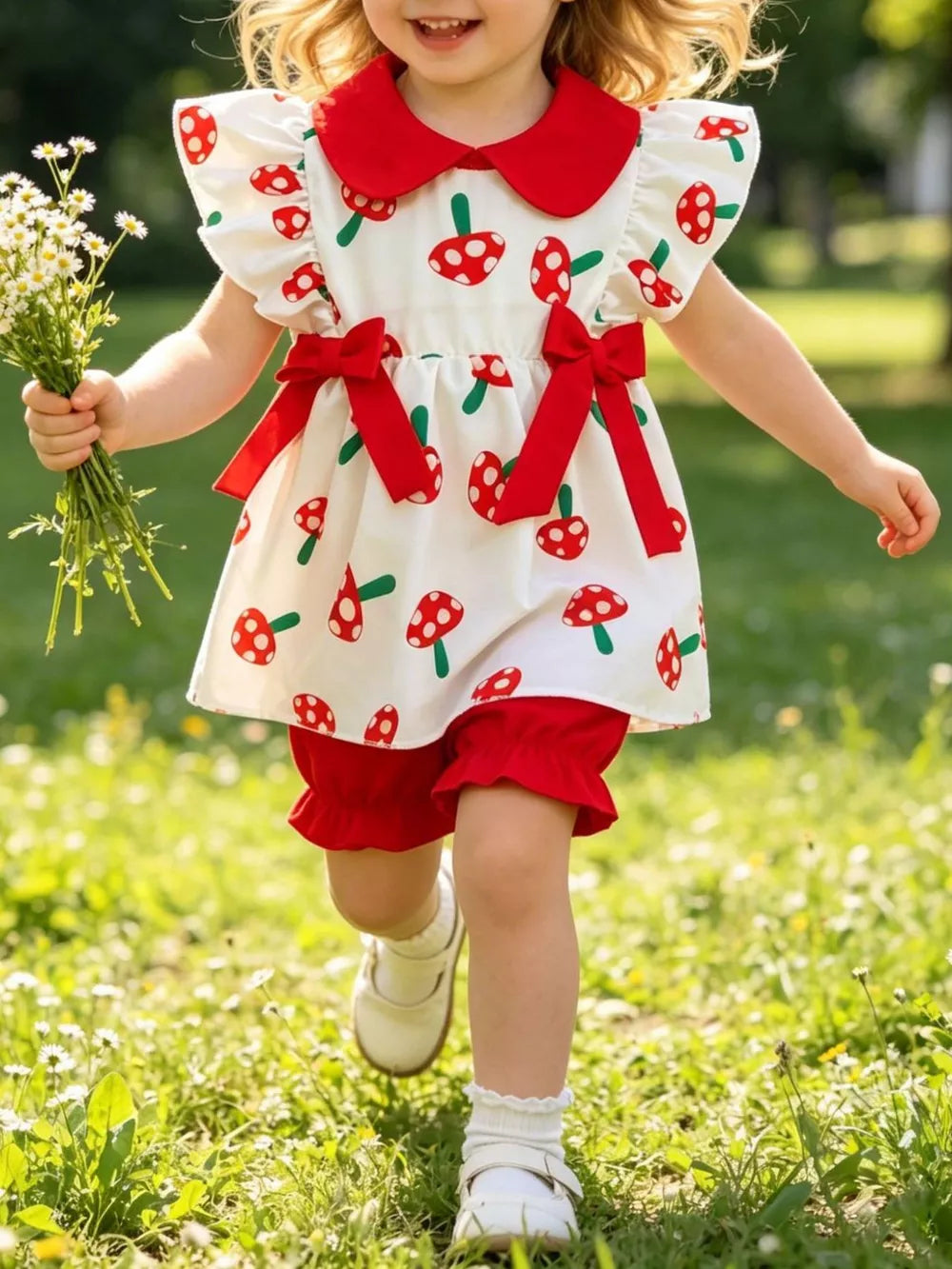 Baby set with red mushroom print, red collar, flutter sleeves, red bows, and ruffled red bloomers.