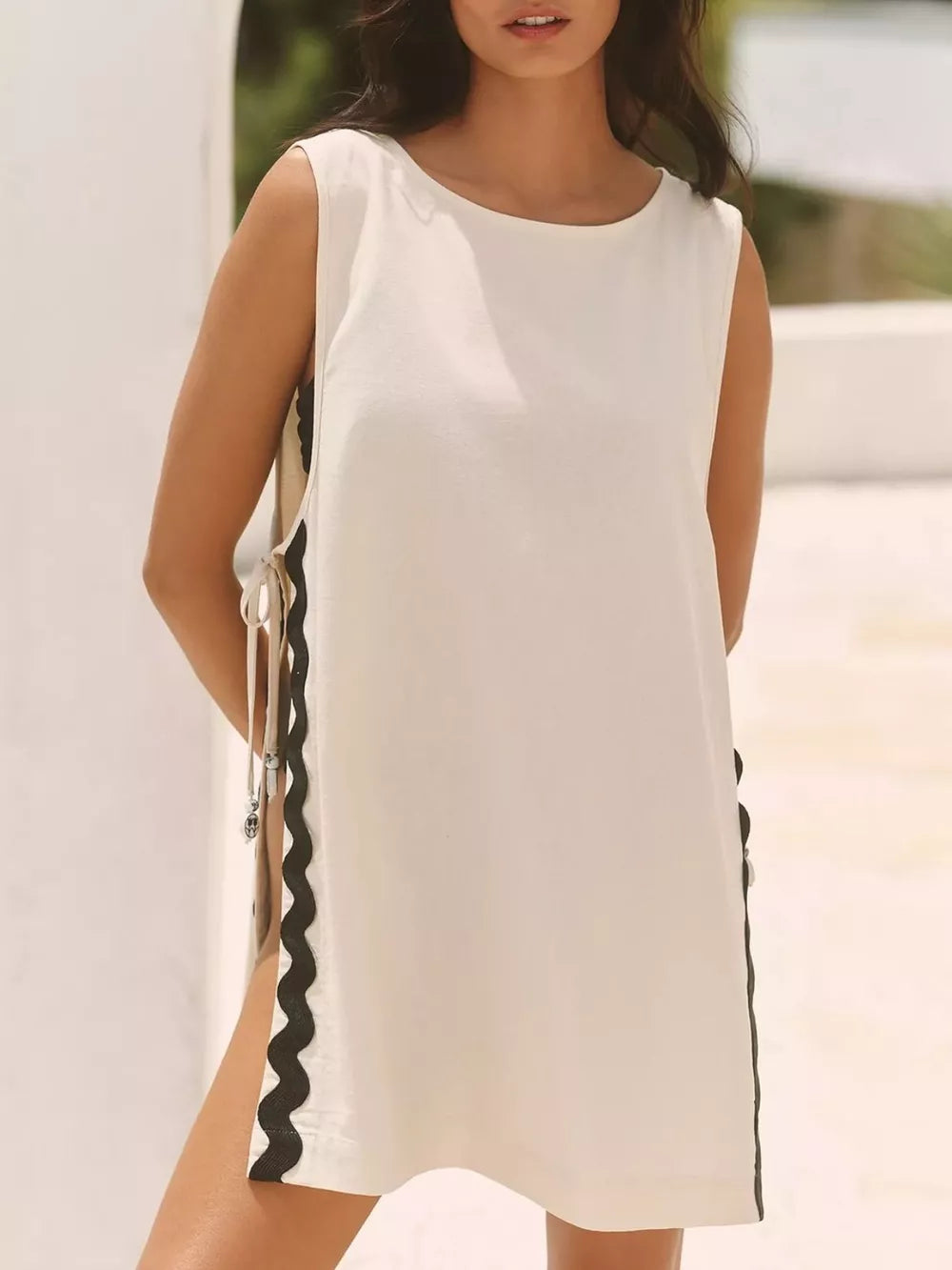 Cream sleeveless mini dress with black scalloped trim and tie details on the sides.