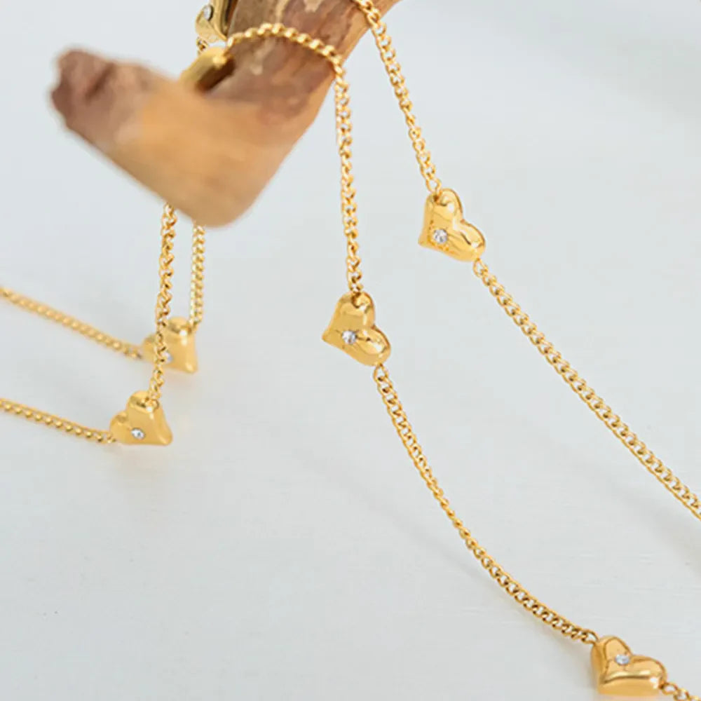 Gold chain necklace with multiple small heart charms and clear stones.