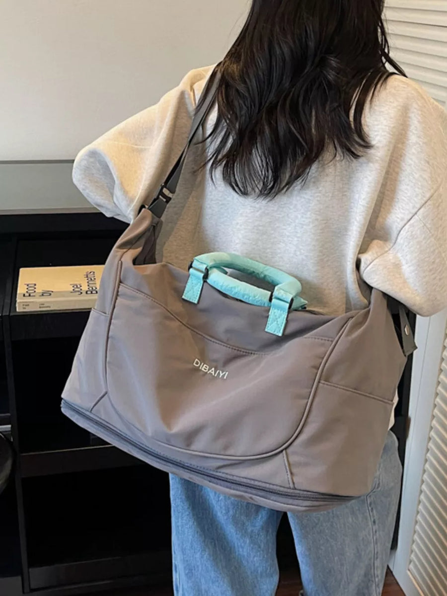 Gray oxford cloth travel duffel bag with light blue handles and a zippered bottom compartment.