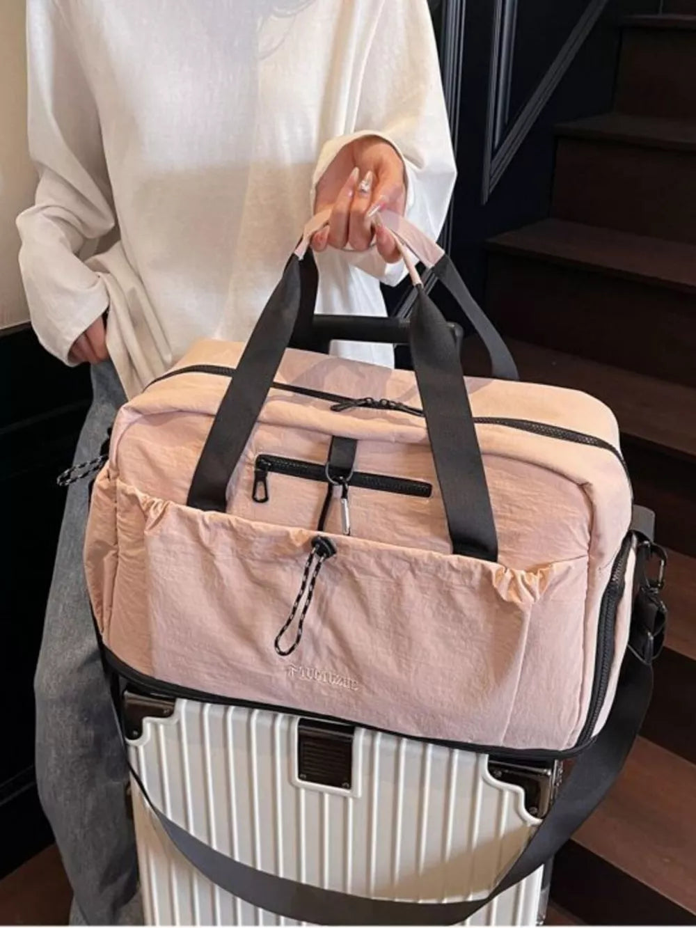 Blush pink lightweight travel duffel bag with black straps and zippers, featuring multiple pockets.