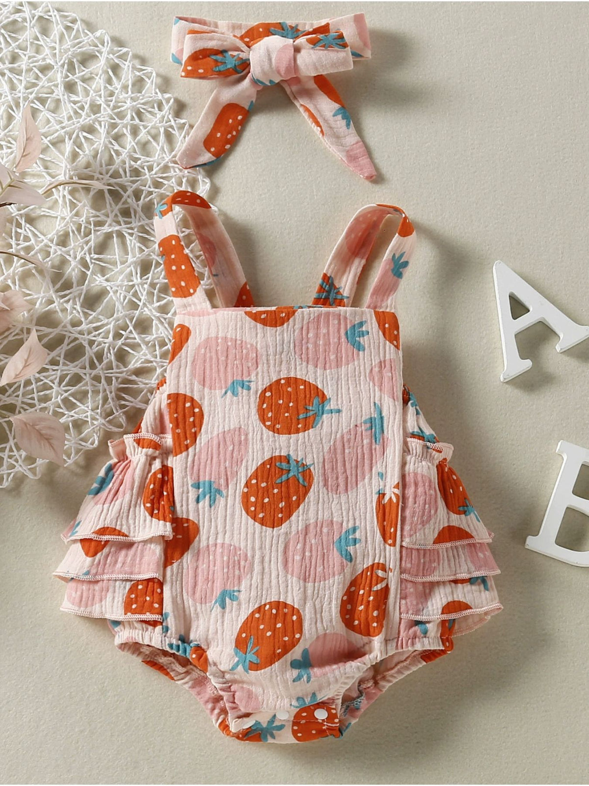 Strawberry print baby bodysuit with ruffled legs and matching headband.