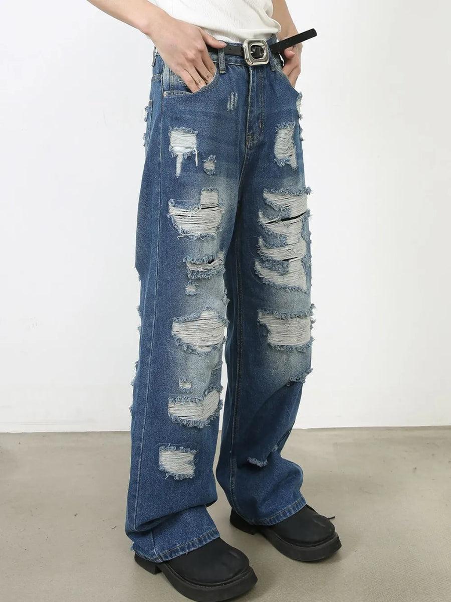 Oversized ripped denim jeans in medium wash with raw edge details and distressed accents.