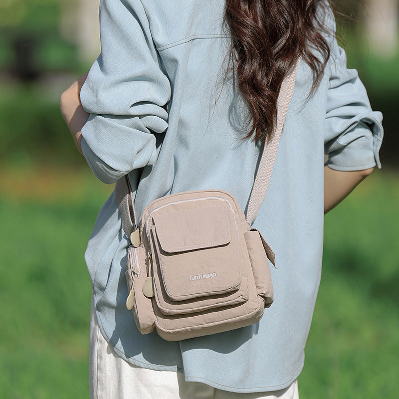 Lightweight tan nylon crossbody bag with multiple pockets and adjustable strap.