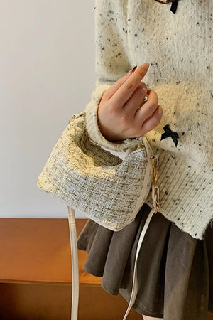 Tweed box bag with gold flecks and detachable strap, held by a hand.