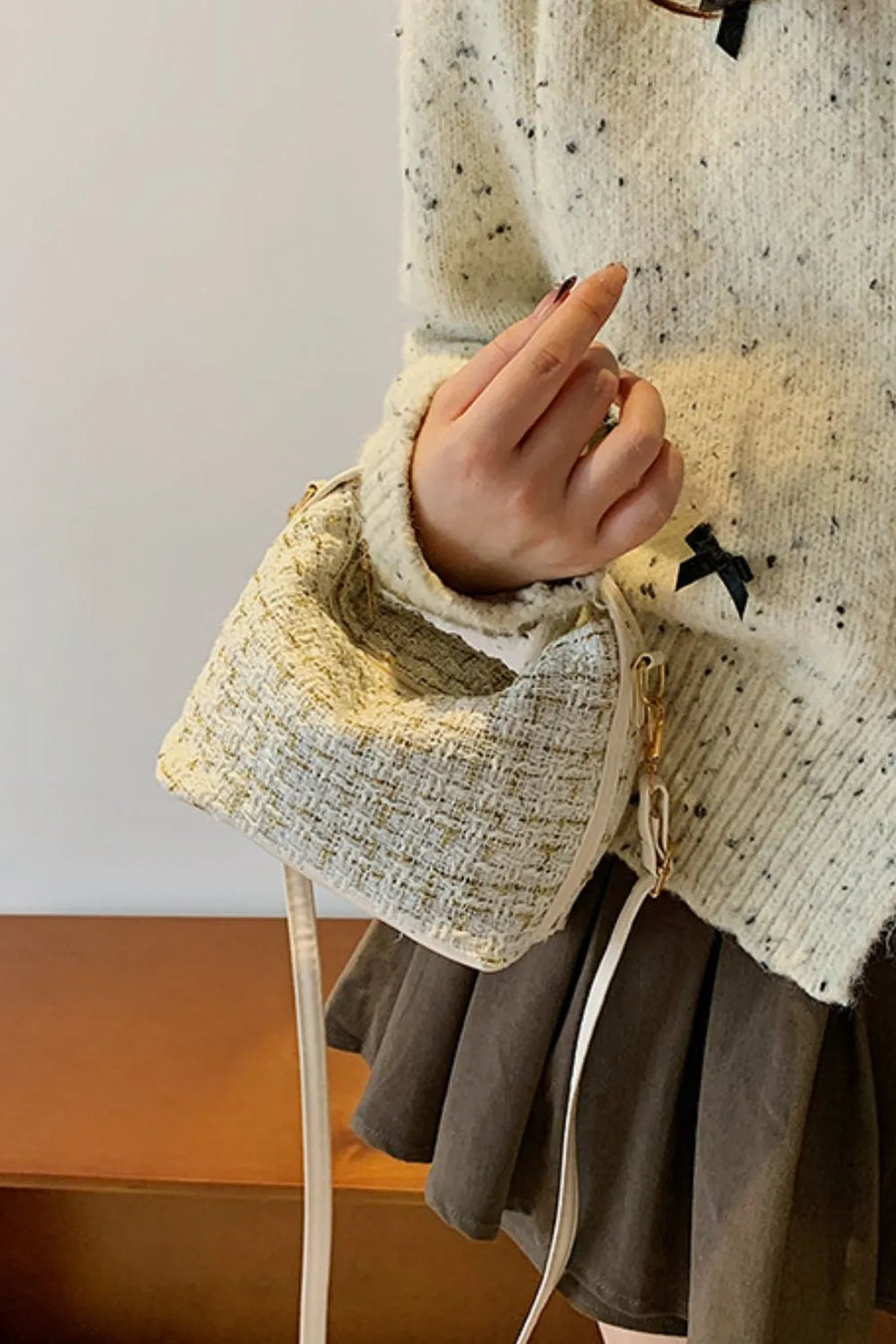Tweed box bag with gold flecks and detachable strap, held by a hand.