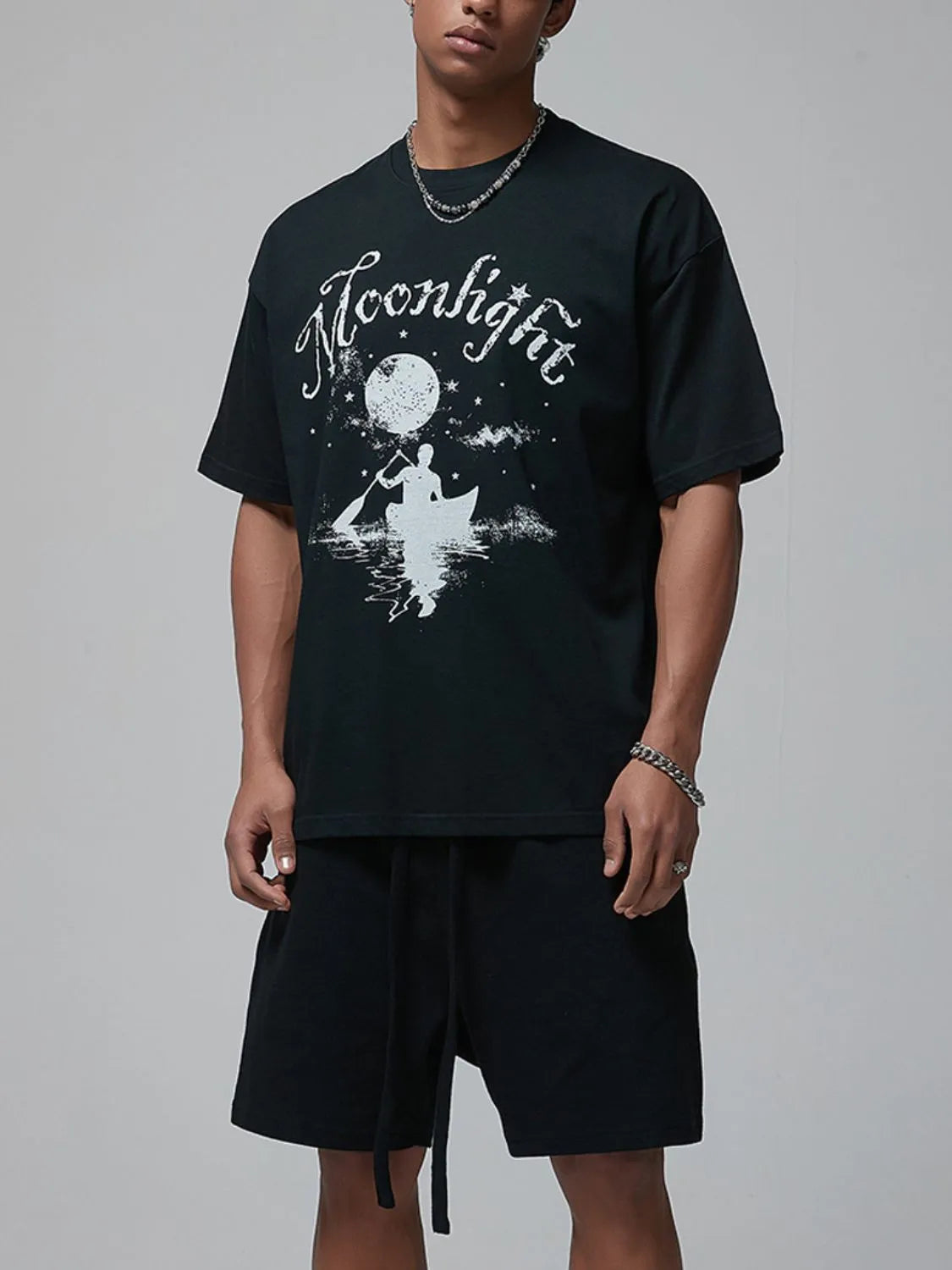 Black oversized tee with white "Moonlight" graphic of a person in a canoe under the moon.