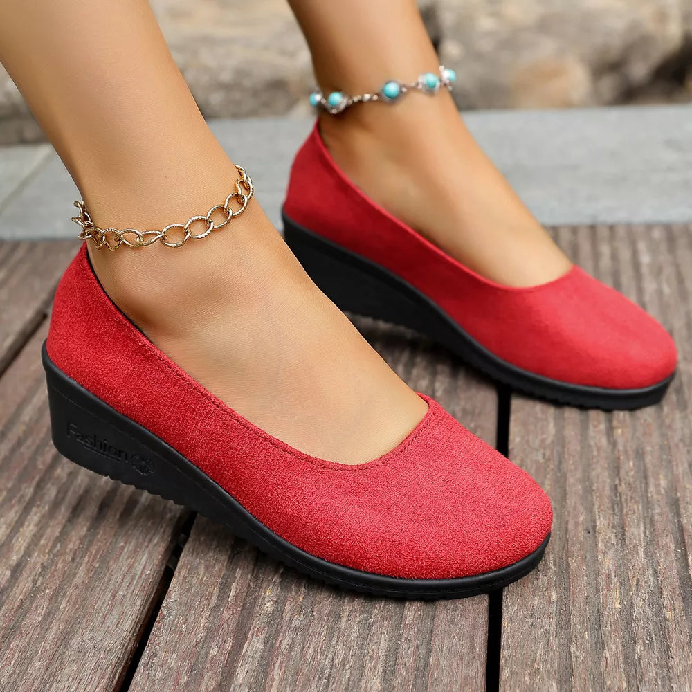 Red textured round toe wedge slip-ons with black soles and ankle chains.
