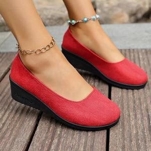 Red textured round toe wedge slip-ons with black soles and ankle chains.