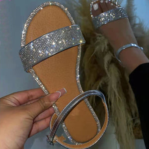 Silver flat ankle sandals with rhinestone-embellished strap and trim.