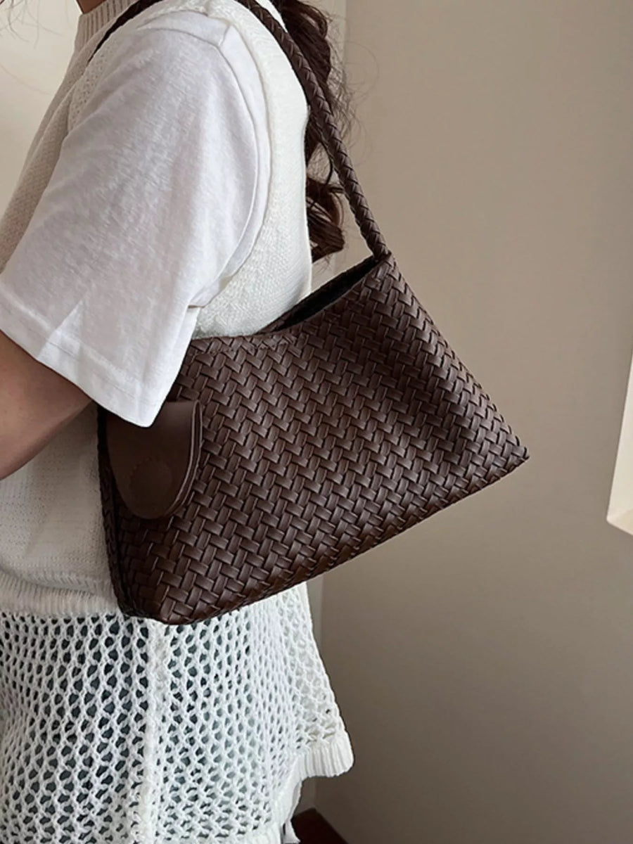 Woven shoulder bag in coffee color with braided strap and flap detail.