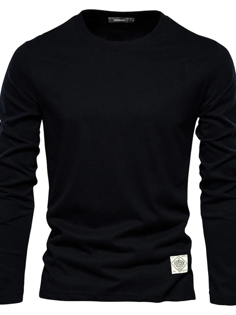 Black crew-neck long-sleeve tee with a textured patch detail on the hem.