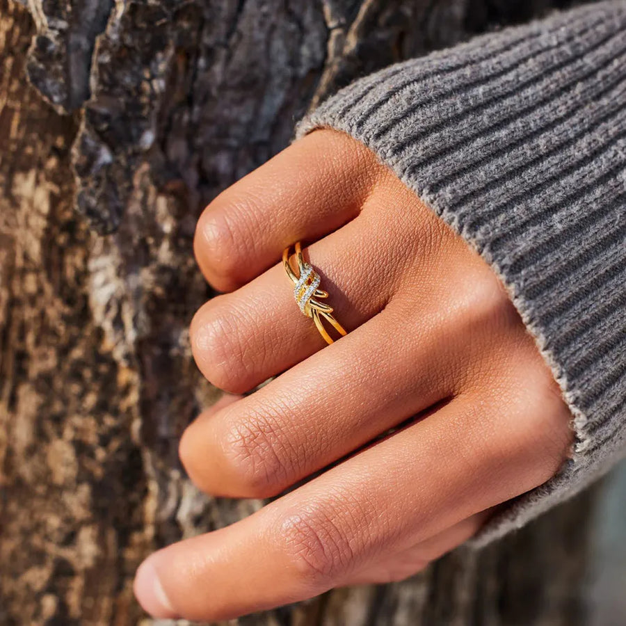 Gold knot ring with diamond accents on a hand wearing a grey sweater.