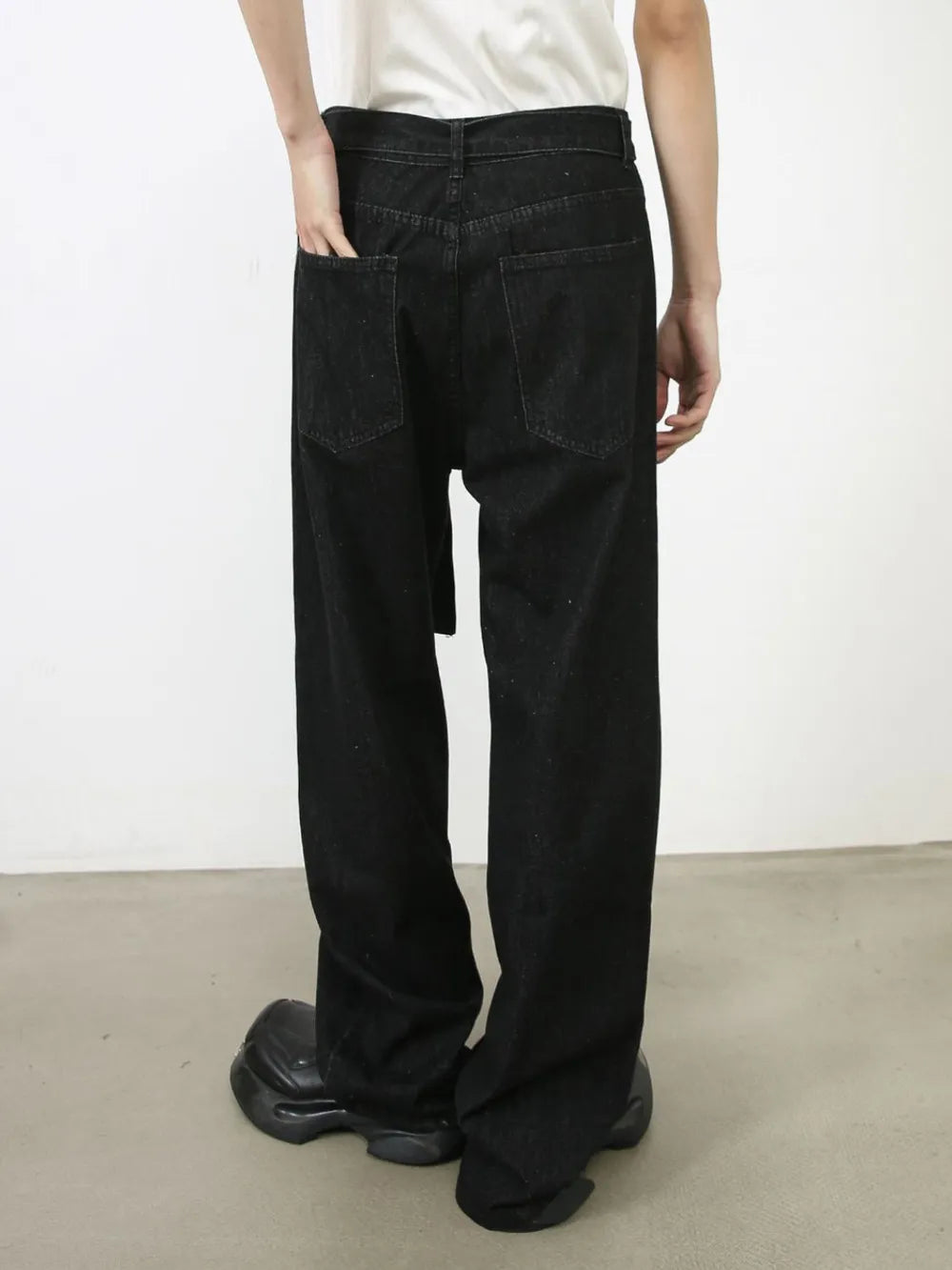 Black wide-leg denim trousers with a belt and sculptural silhouette.