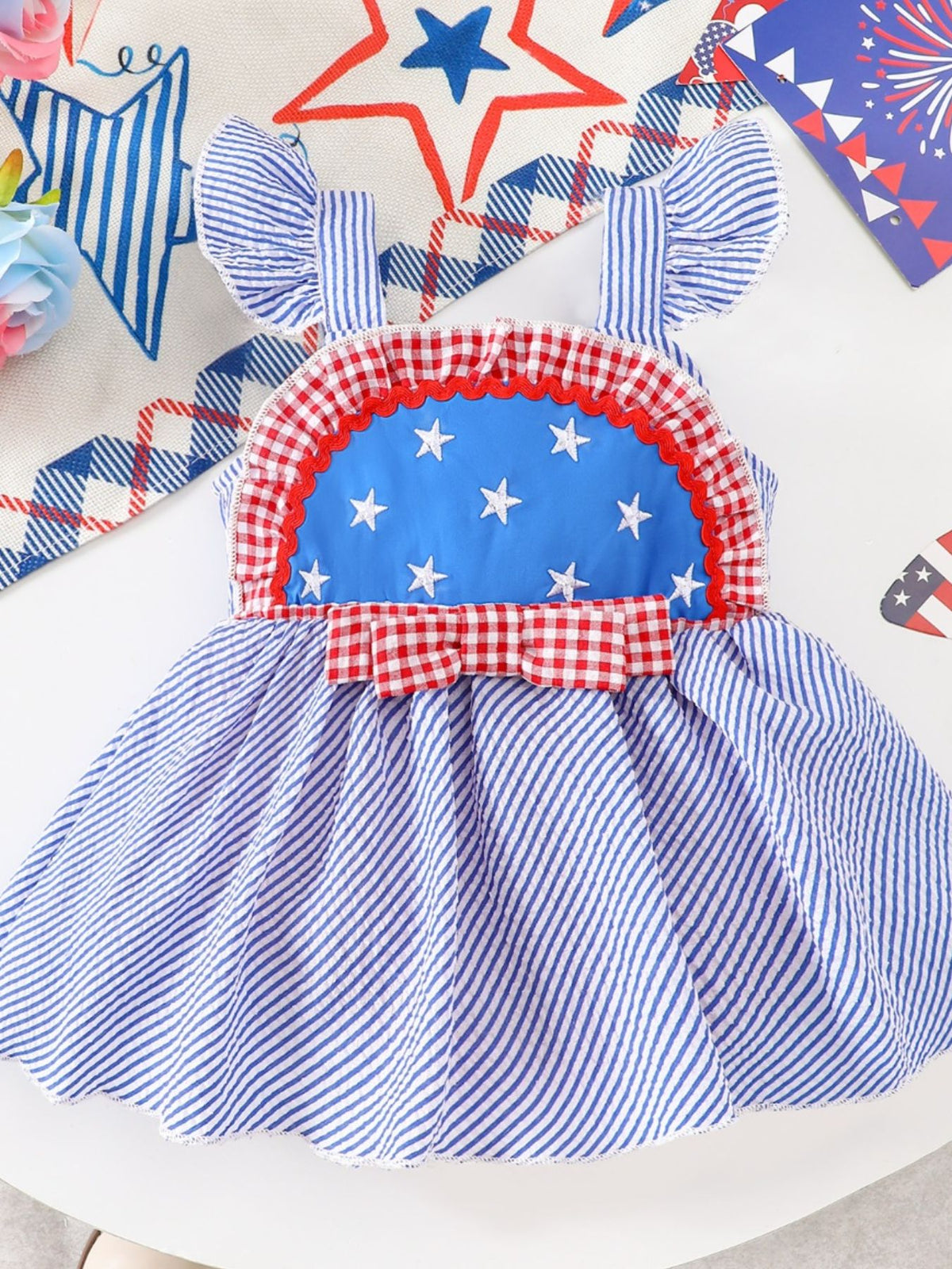 Patriotic baby dress with blue stripes, white stars, red gingham trim, and bow.