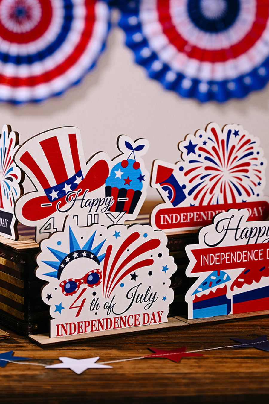Patriotic wooden tabletop decor with USA flag hat, cupcake, fireworks, and Independence Day messages.