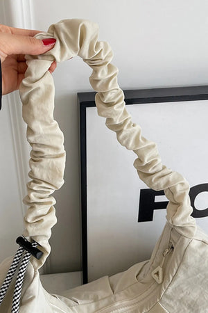 Beige gathered crescent shoulder bag with ruched strap and black and white rope detail.