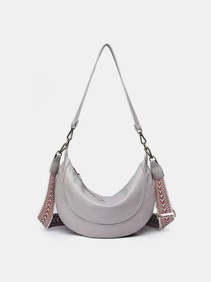 Light gray leather crescent crossbody bag with geometric patterned strap.