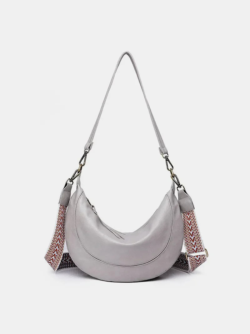 Light gray leather crescent crossbody bag with geometric patterned strap.