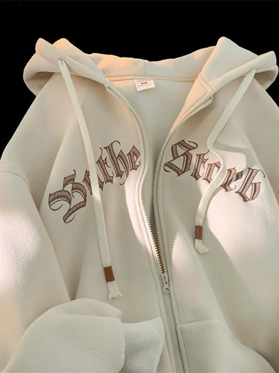 Apricot zip up hoodie with drawstring and gothic text graphic detail.