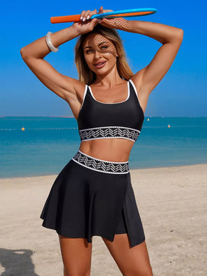 Black tankini swimwear set with white contrast trim and geometric pattern waistband, paired with a black skort.