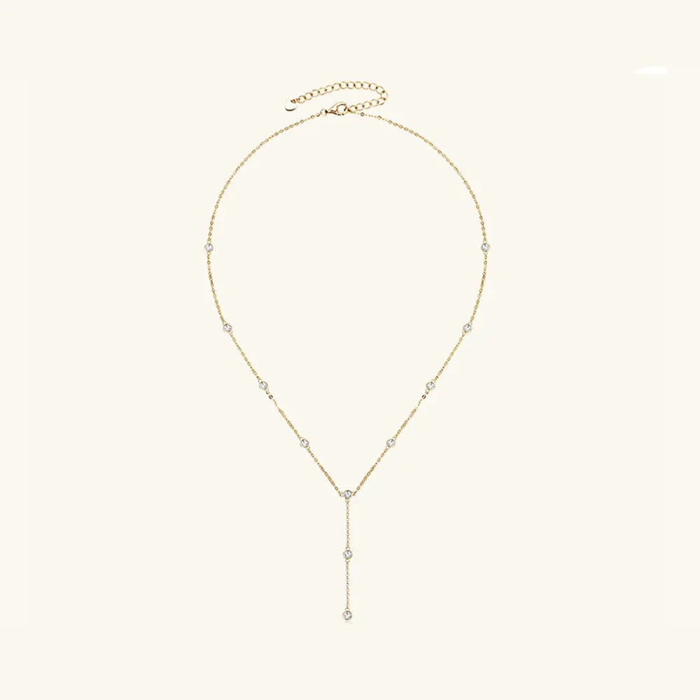 Gold lariat necklace with scattered moissanite stones and a drop pendant.
