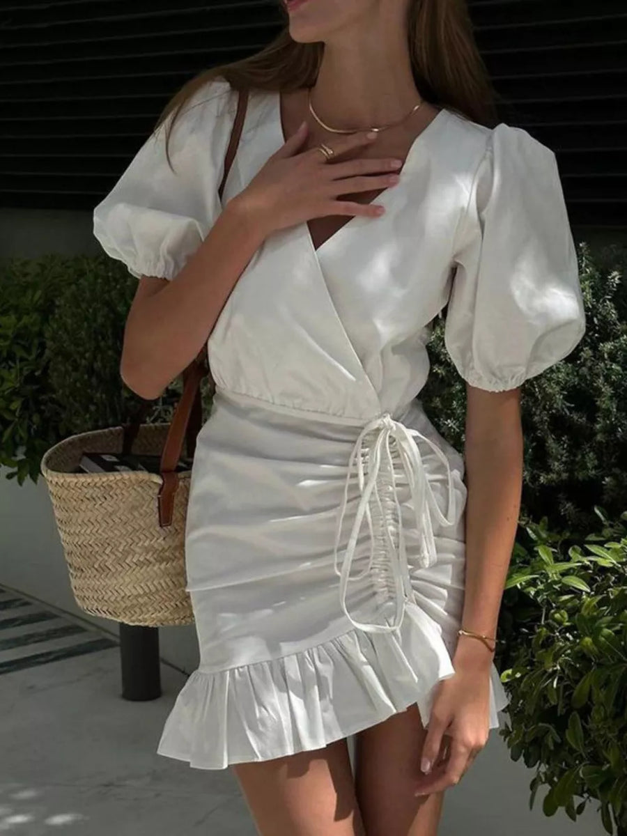 White linen wrap dress with puff sleeves, ruched skirt, and ruffled hem.