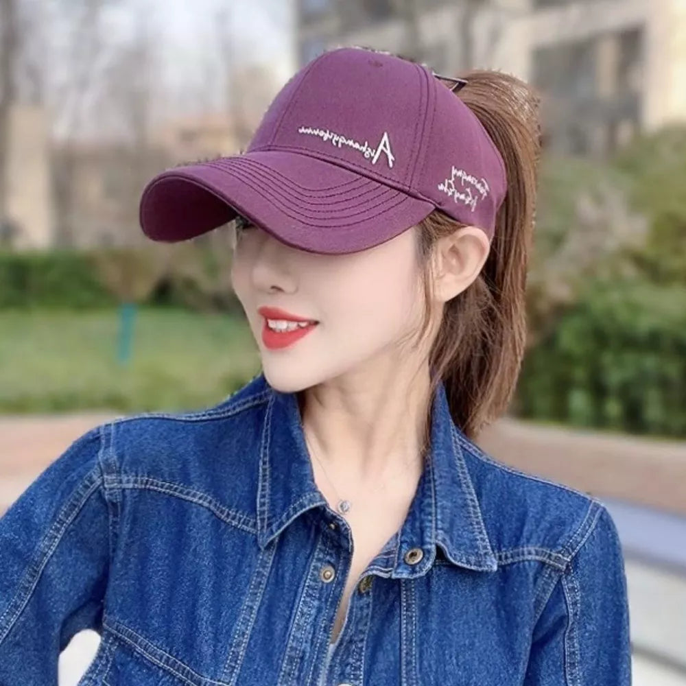 Purple baseball cap with white embroidered 'A' logo and text detail, worn by a woman in a denim jacket.