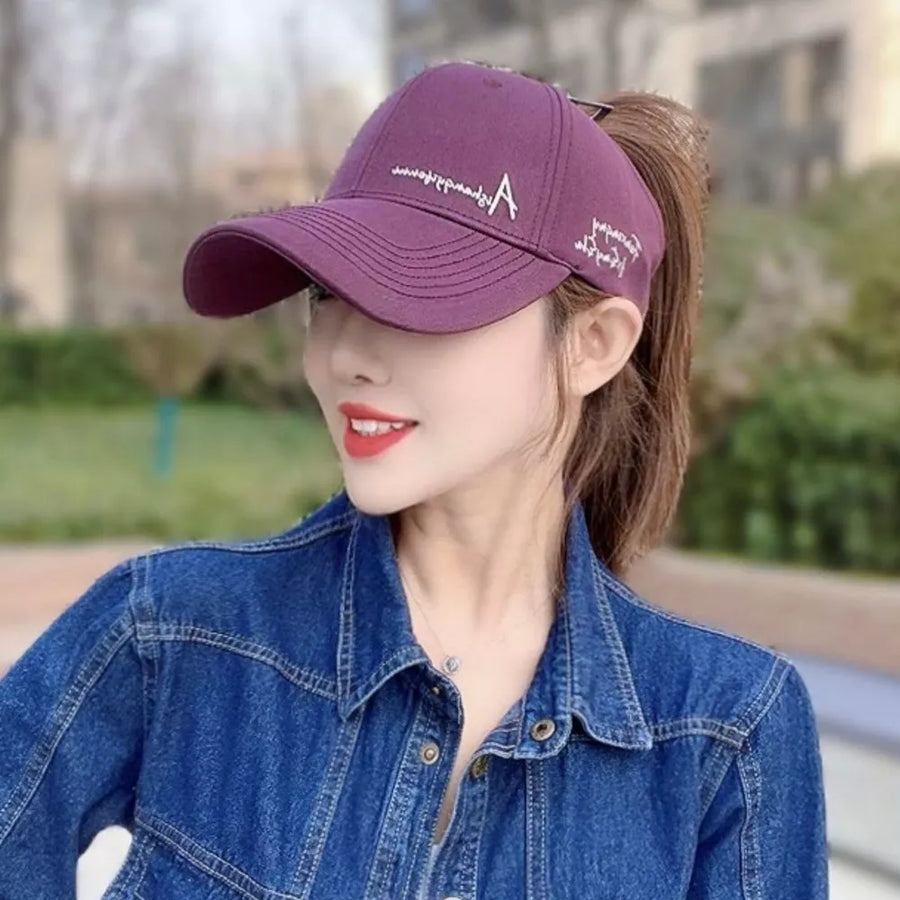 Purple baseball cap with white embroidered 'A' logo and text detail, worn by a woman in a denim jacket.