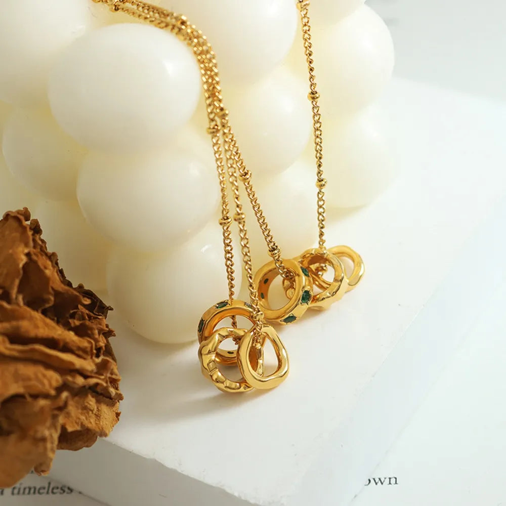 Gold interlocking circle necklace with emerald accents on a delicate chain.