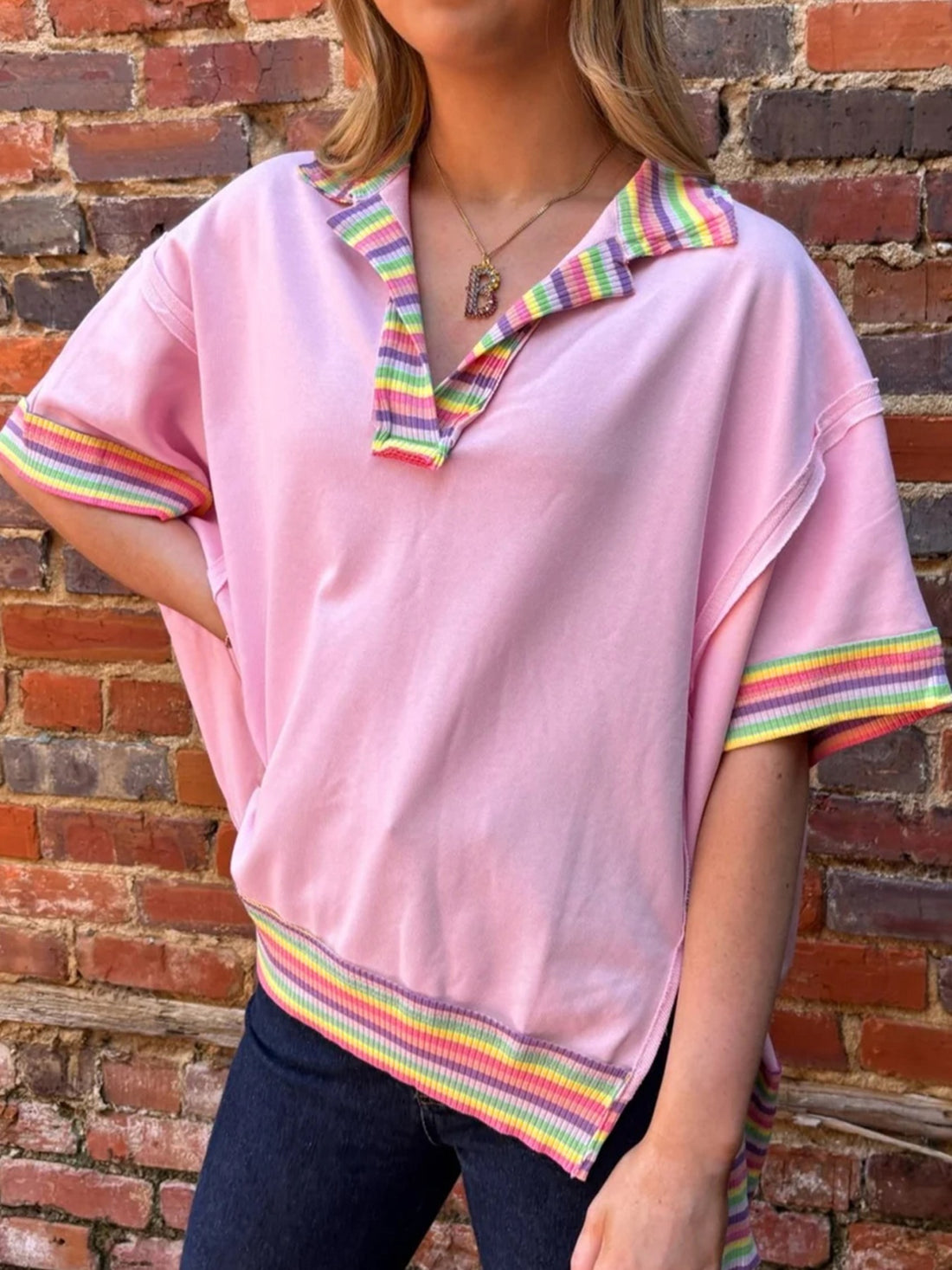 Pink cotton oversized V-neck top with rainbow striped collar, cuffs, and hem.