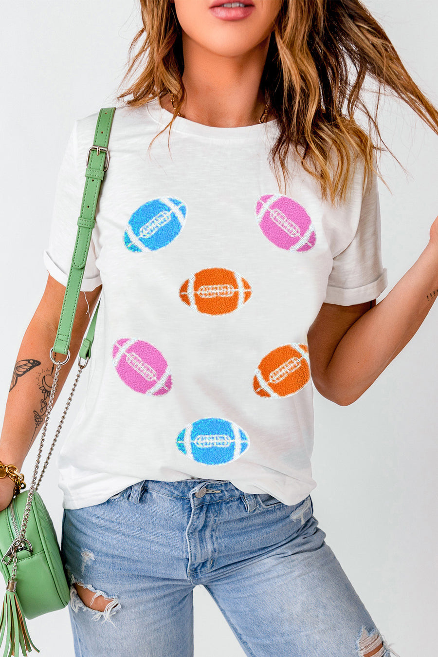 White t-shirt with rolled sleeves and scattered colorful football graphics.