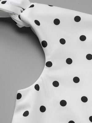 White polka dot mini dress with asymmetrical neckline and bow detail.