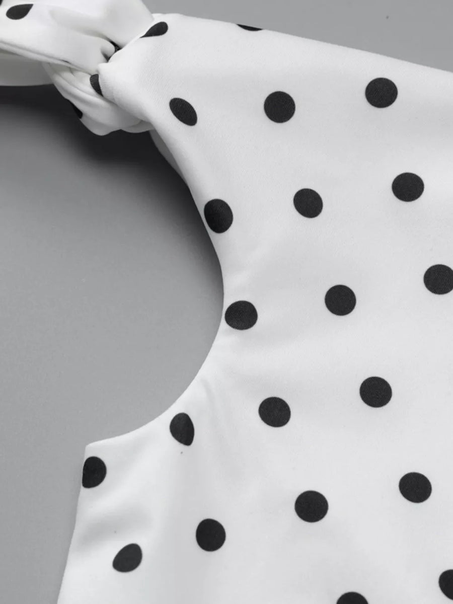 White polka dot mini dress with asymmetrical neckline and bow detail.
