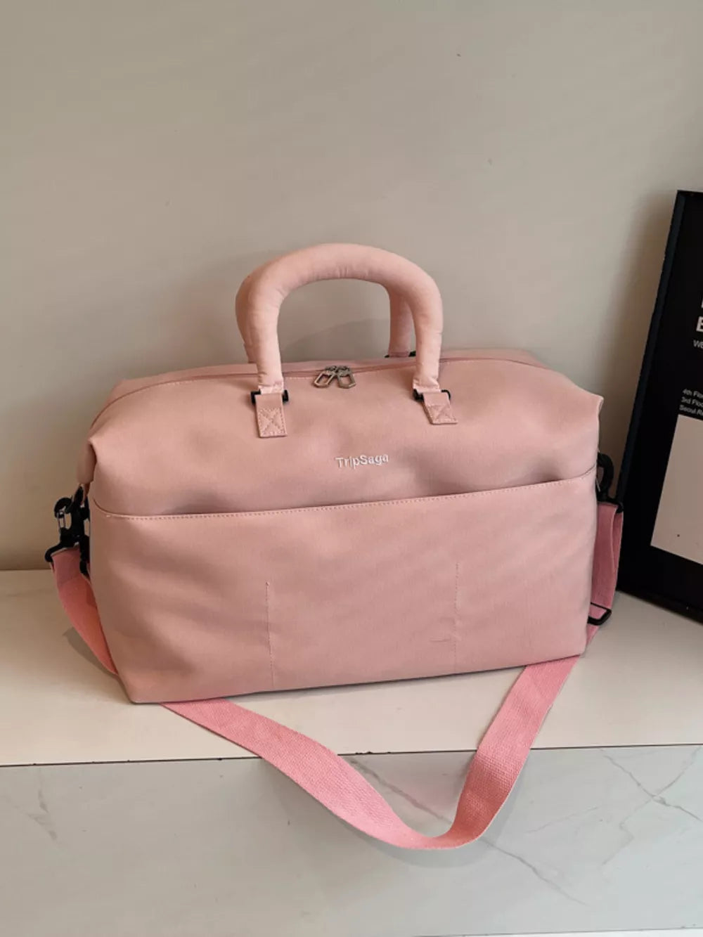 Pink duffel bag with top handles, front pocket, and adjustable strap.