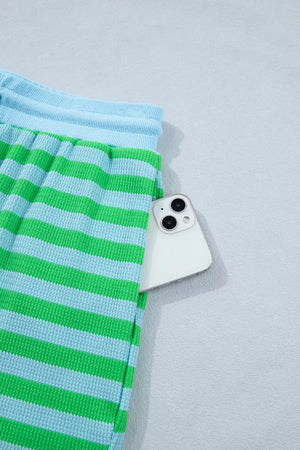 Striped knit shorts in green and light blue with a phone in the pocket.