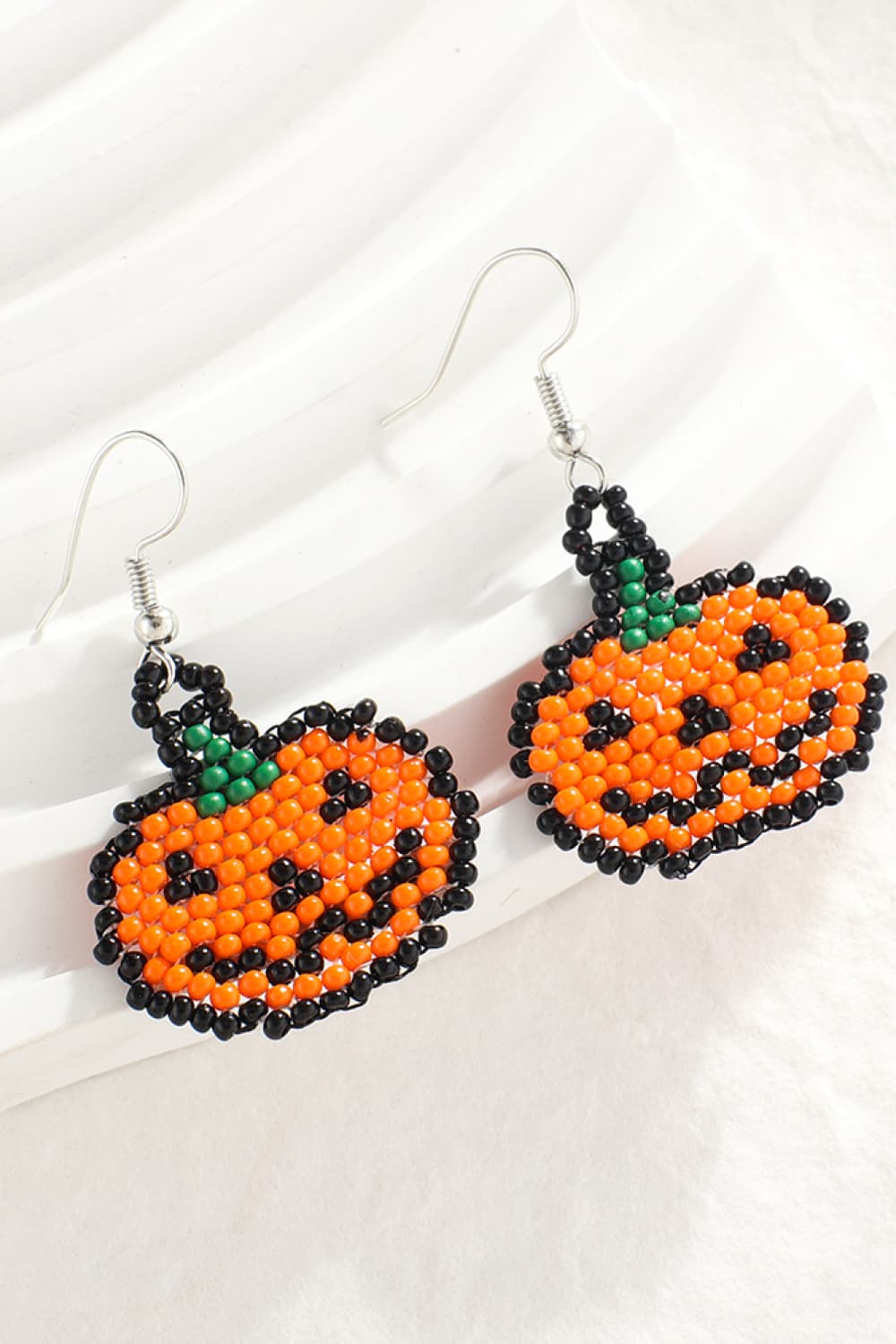 Beaded pumpkin earrings in orange with black and green details, featuring a jack-o'-lantern face.