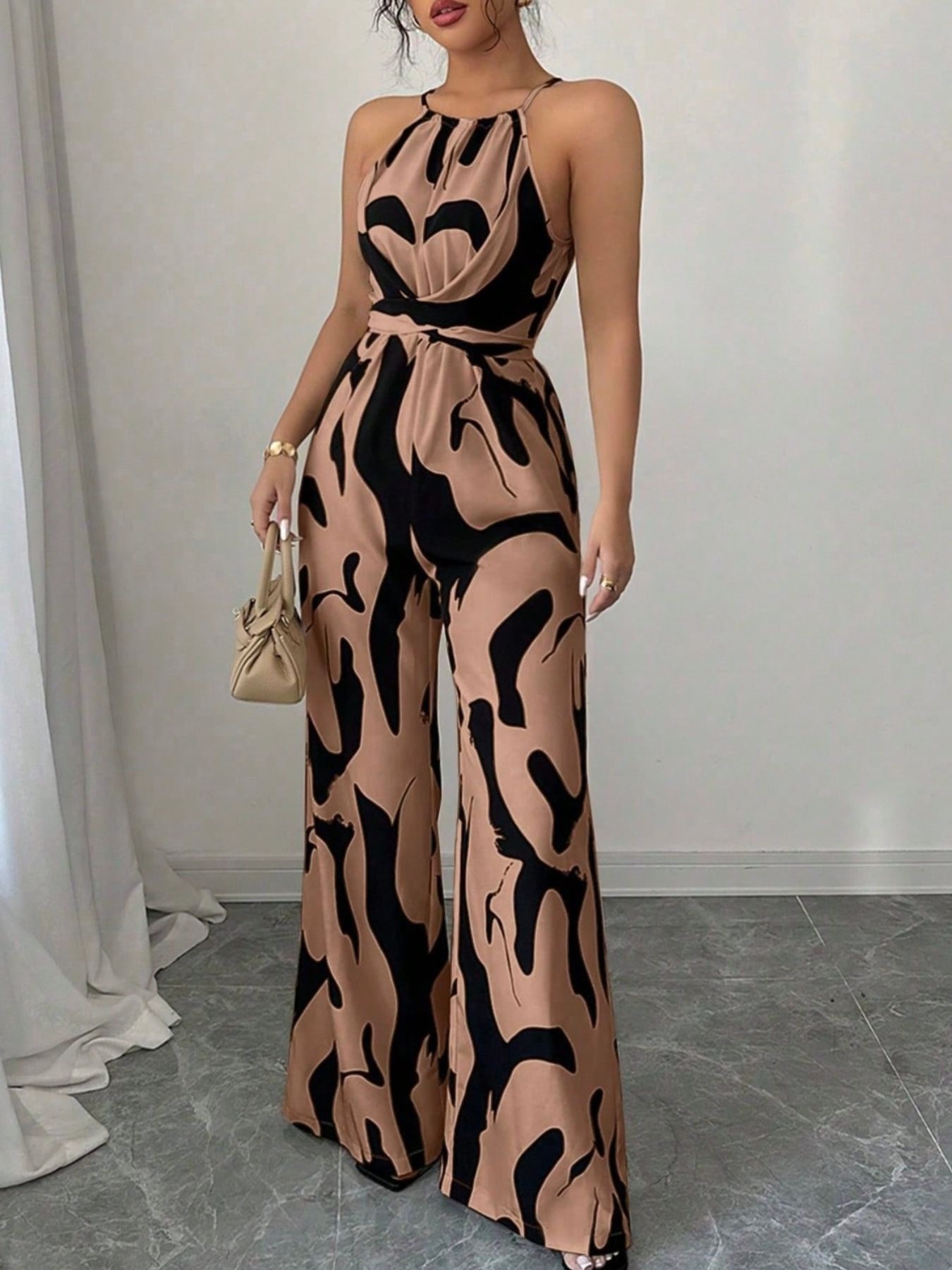 Elegant wide-leg jumpsuit in tan with black abstract print, halter neck, and draped bodice.