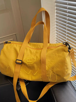 Yellow duffel bag with embroidered smiley face and abstract details, adjustable strap.