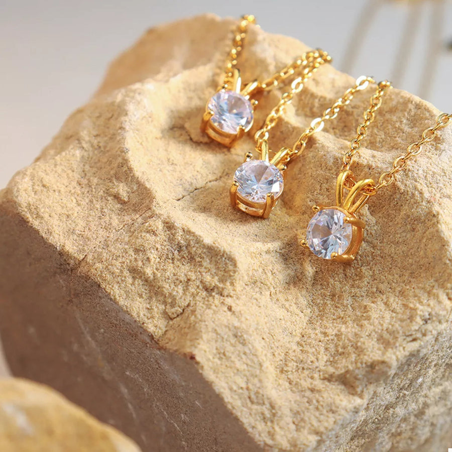 Gold zircon pendant necklaces with delicate chains on a textured stone surface.