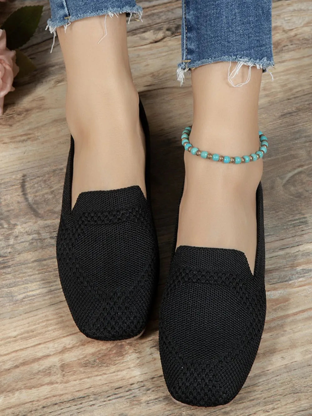 Black knit ballet flats with a textured pattern and a turquoise beaded anklet.